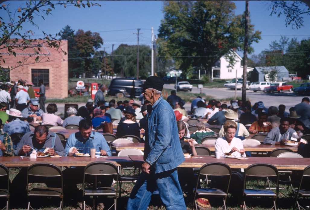 Actors and crew eating lunch in downtown Fort Scott, Kansas. Actor in denim jacket and overalls walks in front.